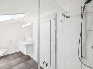 This modern bathroom features a sleek white vanity with a double sink, complemented by a wall-mounted toilet and a spacious glass-enclosed shower.