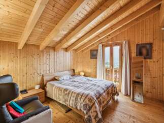 Experience rustic charm in this cozy wooden bedroom, featuring exposed beams and a comfortable bed adorned with a festive deer-themed duvet.