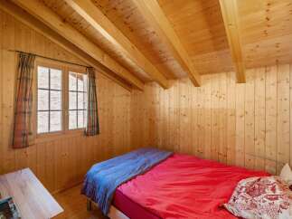 Experience rustic charm in this cozy wooden cabin bedroom, featuring a comfortable bed dressed in vibrant red and blue linens.