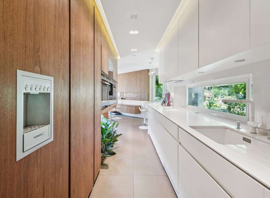 Experience modern luxury in this sleek kitchen, featuring rich wood cabinetry and pristine white countertops.
