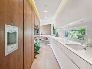 Experience modern luxury in this sleek kitchen, featuring rich wood cabinetry and pristine white countertops.