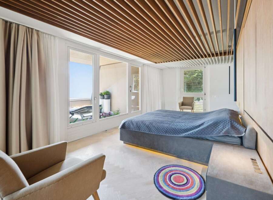 Experience modern luxury in this stunning bedroom featuring a king-size bed with a quilted blue comforter and ambient under-bed lighting.