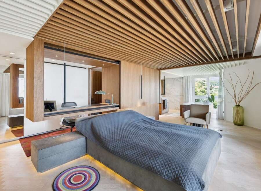Experience modern luxury in this master bedroom featuring a stunning wood-slatted ceiling and integrated desk area.
