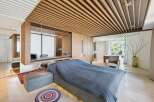 Experience modern luxury in this master bedroom featuring a stunning wood-slatted ceiling and integrated desk area.