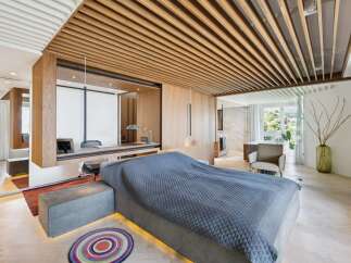 Experience modern luxury in this master bedroom featuring a stunning wood-slatted ceiling and integrated desk area.