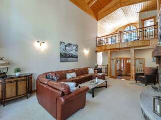 Experience luxury mountain living in this stunning great room, featuring a soaring vaulted wood-beamed ceiling and a grand stone fireplace.