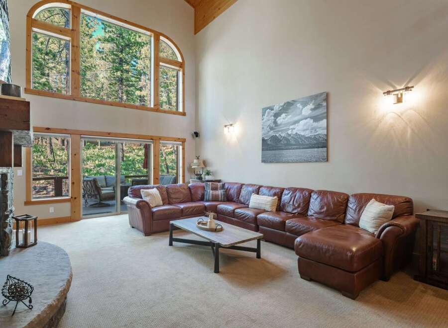 Experience breathtaking mountain views from this stunning living room, featuring a massive arched window and a cozy stone fireplace.