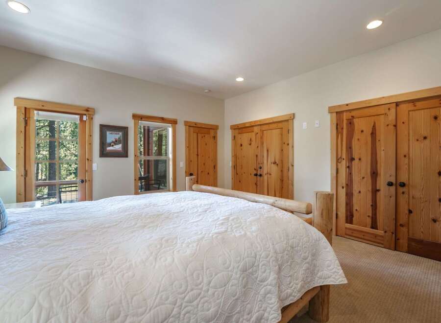 Experience rustic charm in this inviting bedroom, featuring a cozy log-frame bed and ample natural light from large windows overlooking a wooded landscape.