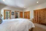 Experience rustic charm in this inviting bedroom, featuring a cozy log-frame bed and ample natural light from large windows overlooking a wooded landscape.
