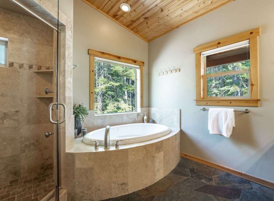 Indulge in relaxation in this luxurious bathroom featuring a spacious corner soaking tub with a scenic forest view.