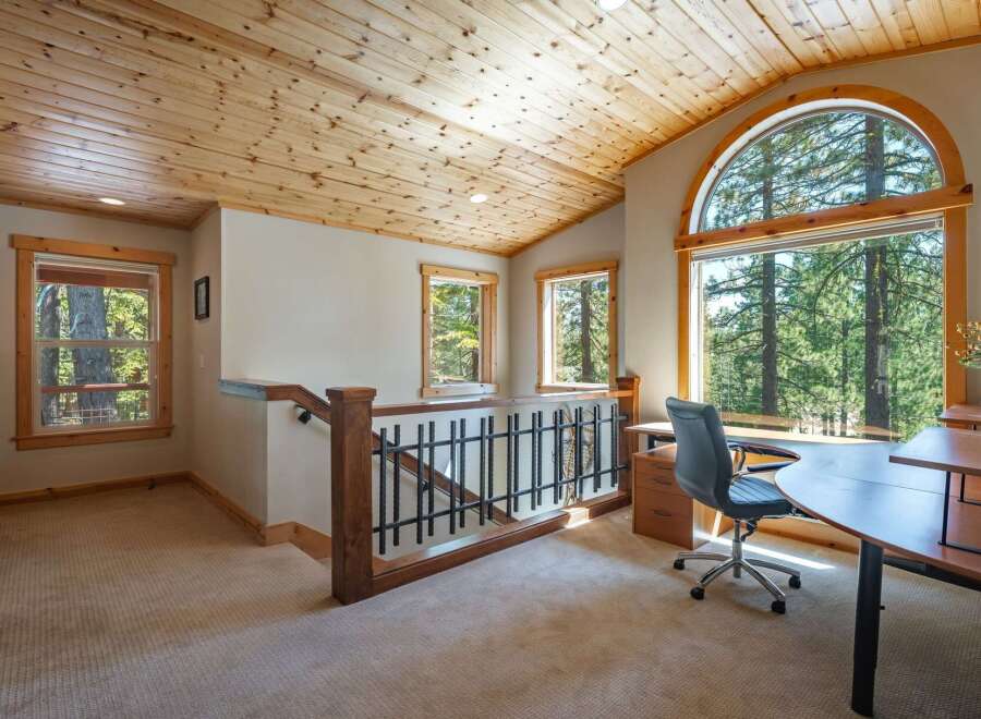 Experience breathtaking forest views from this charming home office, featuring a large arched window that floods the space with natural light.