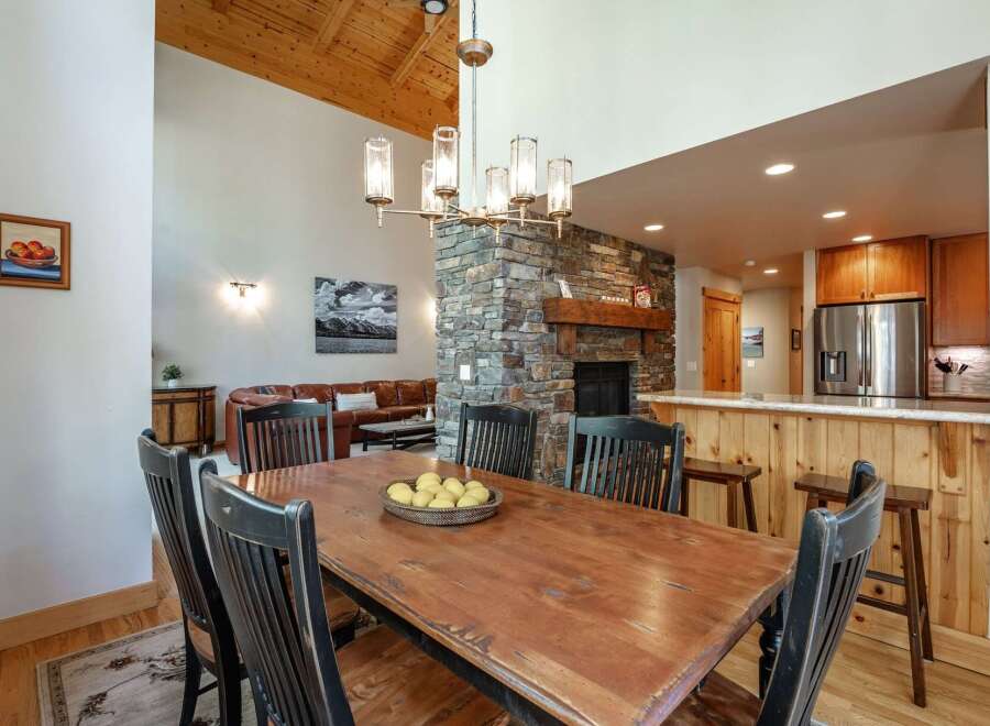 Experience rustic charm in this spacious dining area, featuring a large wooden table perfect for gatherings, complemented by a striking stone fireplace and a vaulted wood-paneled ceiling.
