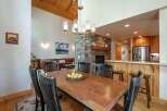 Experience rustic charm in this spacious dining area, featuring a large wooden table perfect for gatherings, complemented by a striking stone fireplace and a vaulted wood-paneled ceiling.