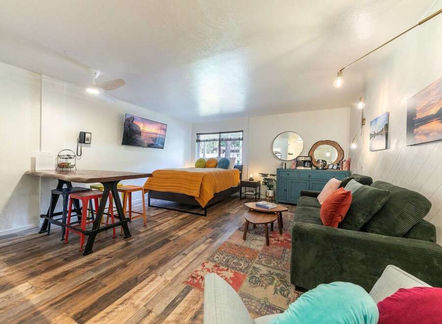 Discover this charming studio apartment featuring a cozy sleeping area with a vibrant orange comforter and plush pillows.