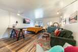 Discover this charming studio apartment featuring a cozy sleeping area with a vibrant orange comforter and plush pillows.