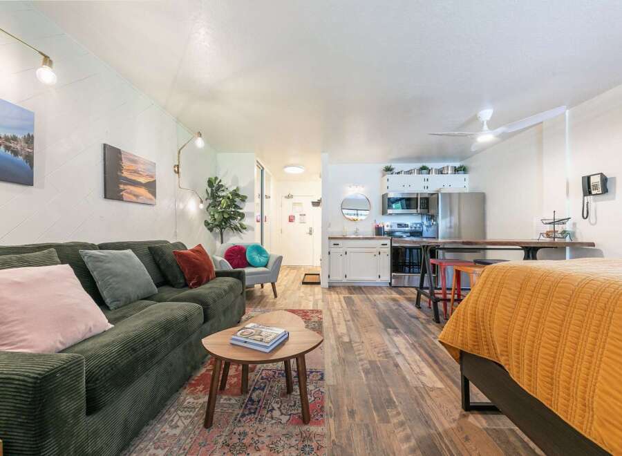 Experience comfortable living in this studio apartment featuring a plush green corduroy sofa and a cozy bed with a vibrant orange quilt.