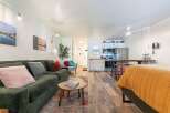 Experience comfortable living in this studio apartment featuring a plush green corduroy sofa and a cozy bed with a vibrant orange quilt.