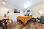 Experience comfort and style in this inviting bedroom, featuring a plush bed adorned with a vibrant orange quilt and decorative pillows.
