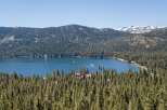 Experience the ultimate lakeside living with this stunning aerial view of a serene blue lake surrounded by lush green pine forests.