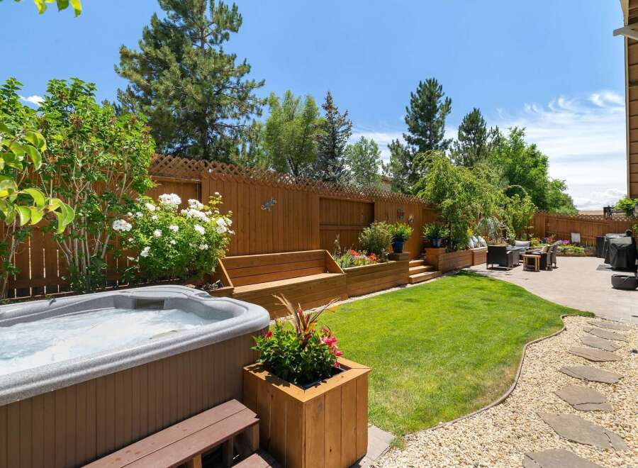 Escape to your private backyard oasis, featuring a luxurious hot tub perfect for relaxation and a beautifully landscaped garden with tiered wooden planters and a built-in bench.