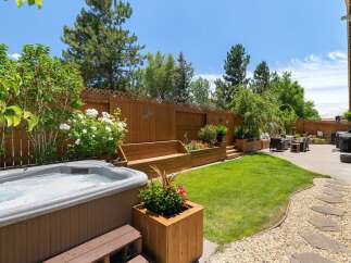 Escape to your private backyard oasis, featuring a luxurious hot tub perfect for relaxation and a beautifully landscaped garden with tiered wooden planters and a built-in bench.