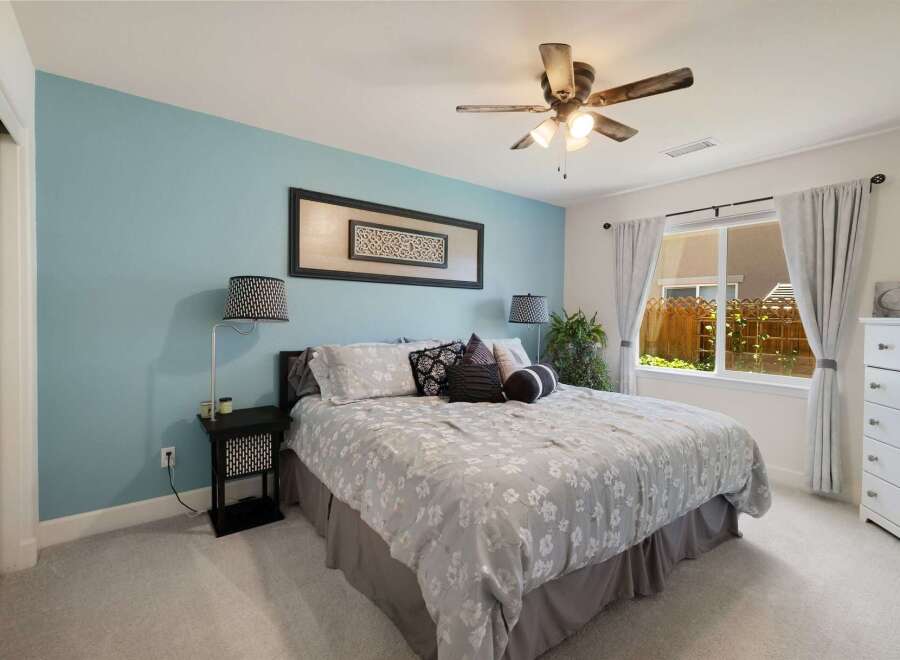 This inviting bedroom features a calming blue accent wall and a comfortable queen-sized bed adorned with a floral comforter and decorative pillows.