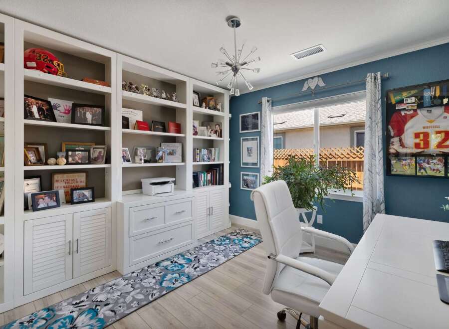 This home office features a large built-in white bookshelf filled with personal mementos and books, complemented by a stylish floral runner rug.