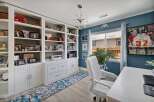 This home office features a large built-in white bookshelf filled with personal mementos and books, complemented by a stylish floral runner rug.