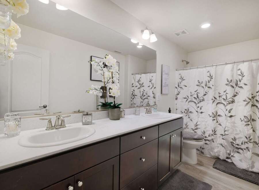 This modern bathroom features a spacious double vanity with dark wood cabinets and a white quartz countertop, offering ample storage and a sleek look.