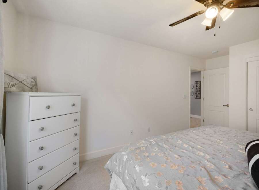 Discover comfort and style in this inviting bedroom, featuring a pristine white dresser adorned with decorative knobs and a charming 'love' sign.
