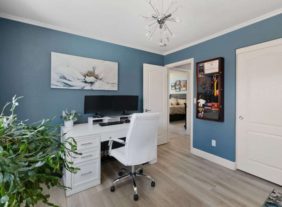This home office features a serene blue wall adorned with a striking floral art piece, complemented by a modern white desk and chair setup.