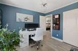 This home office features a serene blue wall adorned with a striking floral art piece, complemented by a modern white desk and chair setup.