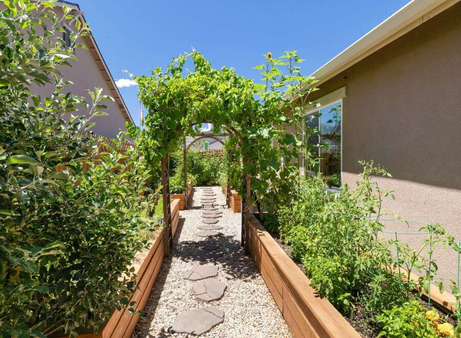 Discover this charming backyard oasis featuring a picturesque garden path lined with raised garden beds, perfect for cultivating your own produce.