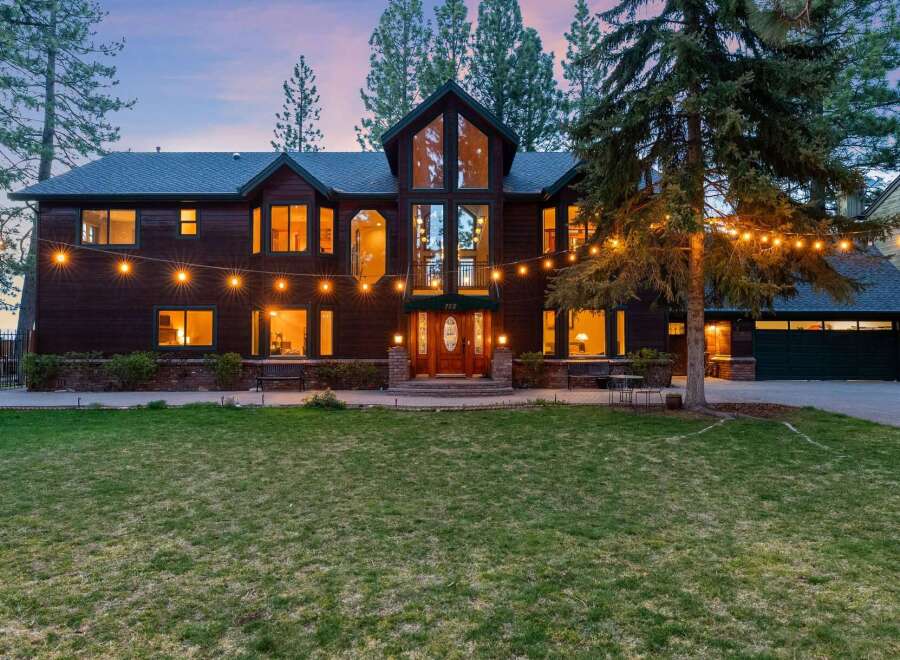 Experience luxury living in this stunning dark wood-sided home, illuminated by warm interior lights and festive string lights.