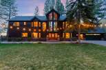 Experience luxury living in this stunning dark wood-sided home, illuminated by warm interior lights and festive string lights.
