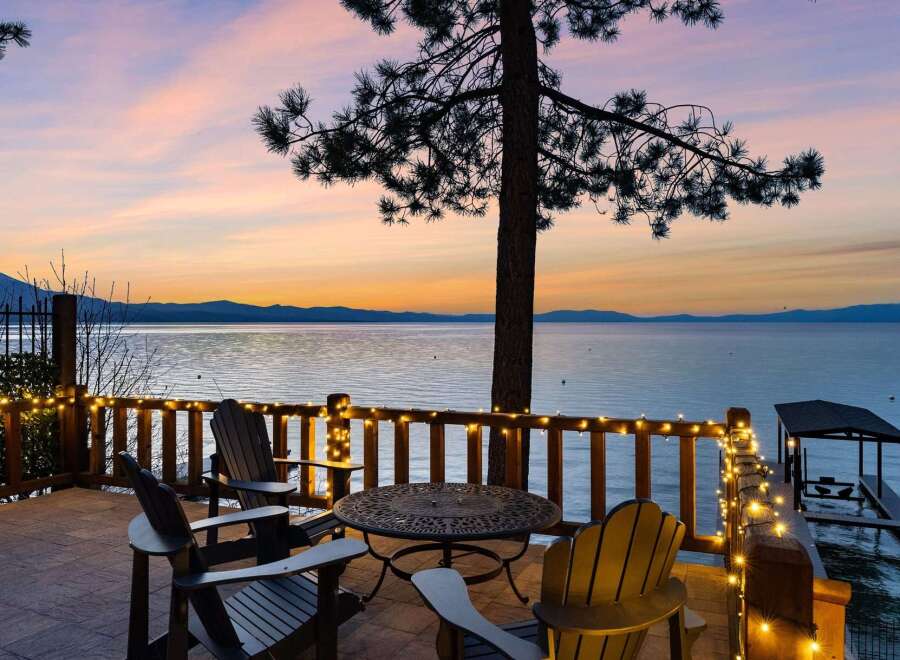 Experience breathtaking sunset views from this stunning lakefront property's expansive deck, complete with cozy Adirondack chairs and charming string lights.