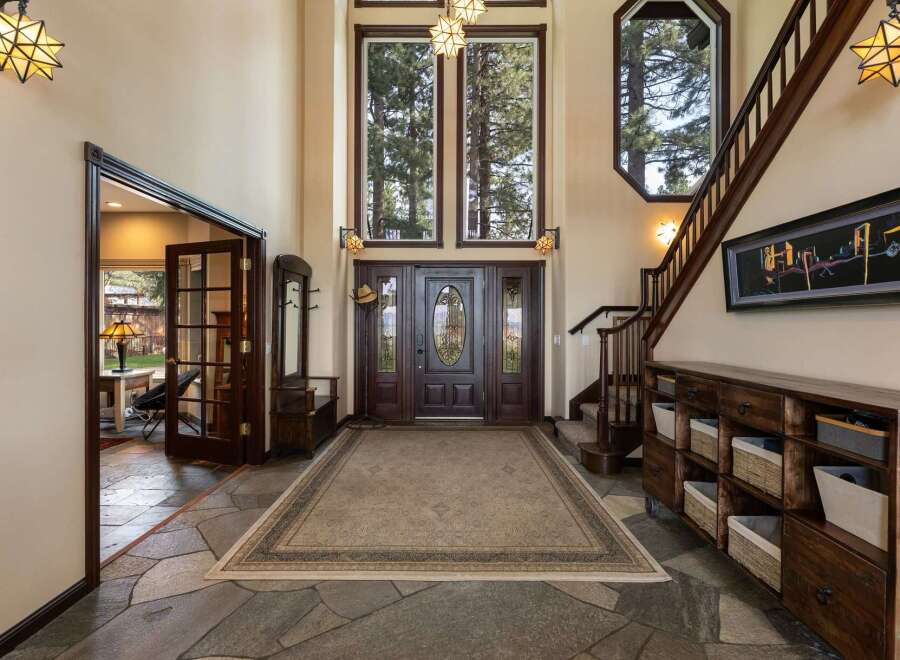 Step into a grand foyer featuring a stunning double-door entrance with intricate glass inlays, leading to a spacious living area.