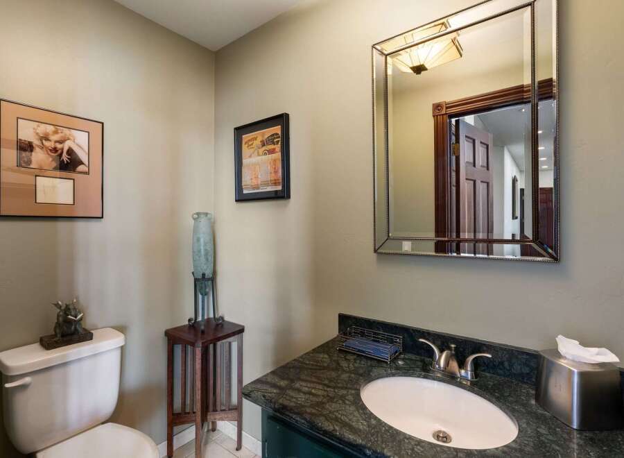 This powder room offers a sophisticated ambiance with its elegant vanity featuring a dark green cabinet and a striking marble countertop.