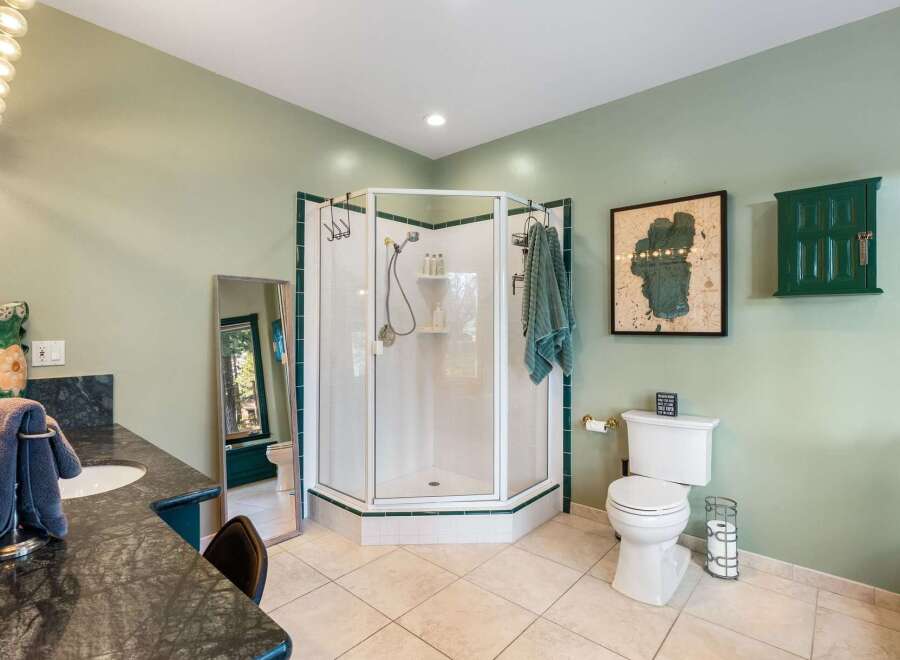 This spacious bathroom features a large corner shower with glass doors and white tiled walls, complemented by elegant green trim.