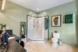 This spacious bathroom features a large corner shower with glass doors and white tiled walls, complemented by elegant green trim.