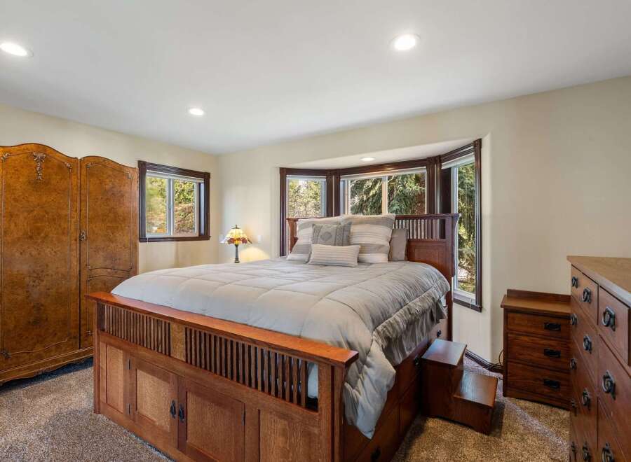 Experience rustic charm in this inviting bedroom, featuring a substantial wooden bed frame with integrated storage and a beautiful bay window overlooking lush greenery.