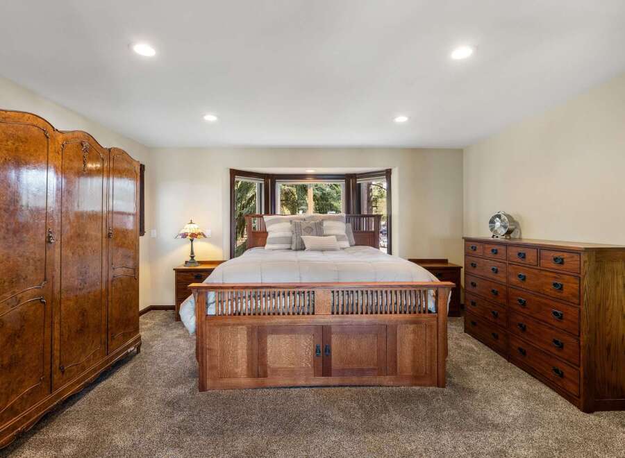 Experience rustic charm in this spacious bedroom, featuring a grand wooden bed frame and a large bay window overlooking lush greenery.