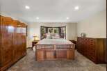 Experience rustic charm in this spacious bedroom, featuring a grand wooden bed frame and a large bay window overlooking lush greenery.