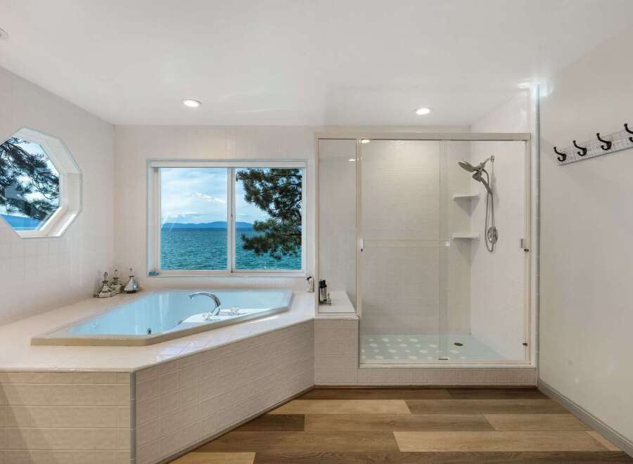 Experience breathtaking lake views from this luxurious bathroom, featuring a spacious soaking tub and a separate glass-enclosed shower.