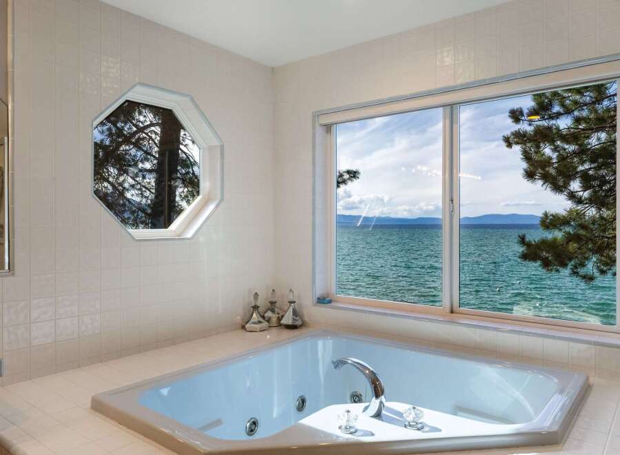 Indulge in ultimate relaxation in this luxurious bathroom featuring a spacious jacuzzi tub with stunning panoramic views of the serene lake and distant mountains.