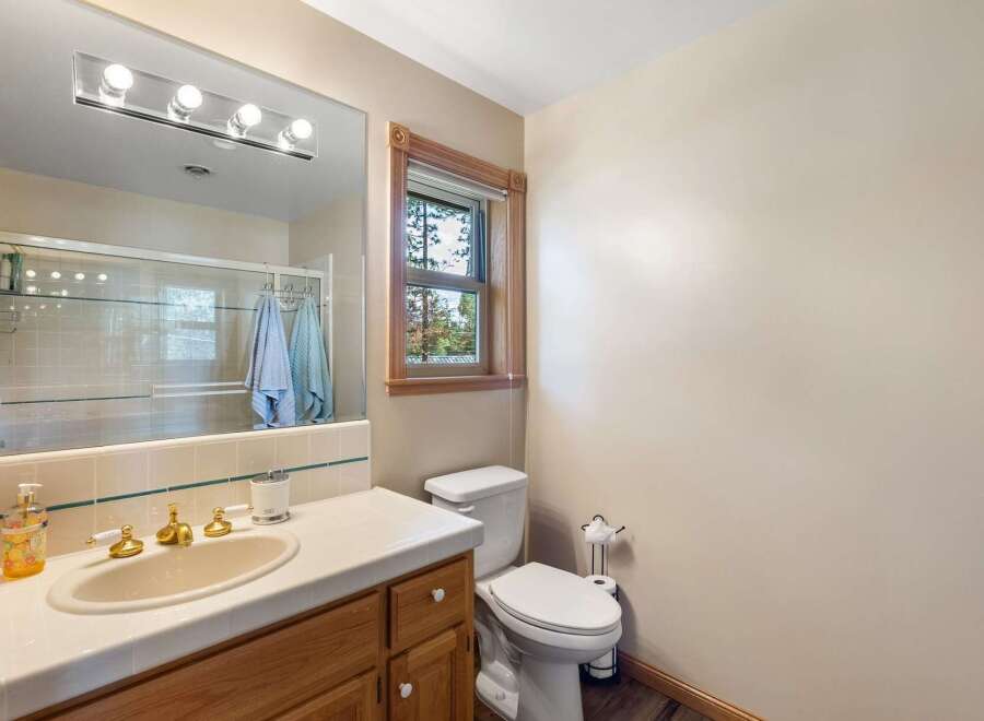 This charming bathroom features a spacious vanity with a gold-toned sink and faucet, complemented by a large mirror with a modern light fixture.