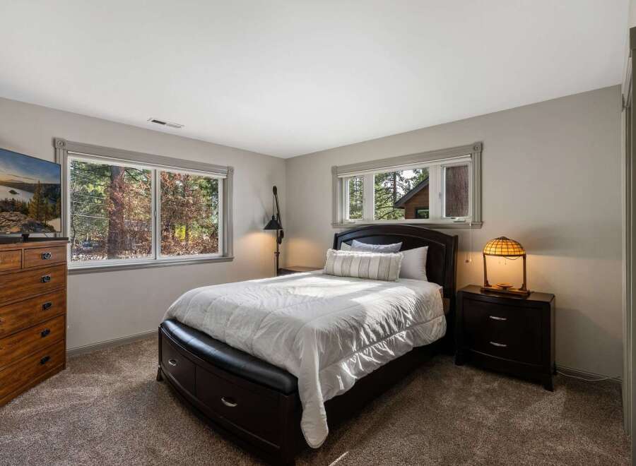 This cozy bedroom offers a tranquil retreat with its plush carpeting and large windows that provide abundant natural light and scenic views of the surrounding trees.