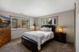 This cozy bedroom offers a tranquil retreat with its plush carpeting and large windows that provide abundant natural light and scenic views of the surrounding trees.