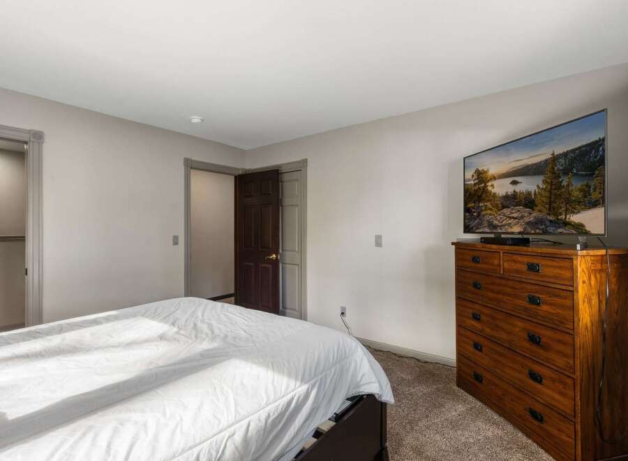 This bedroom offers a comfortable and inviting space with a large bed and a modern flat-screen TV mounted above a wooden dresser.