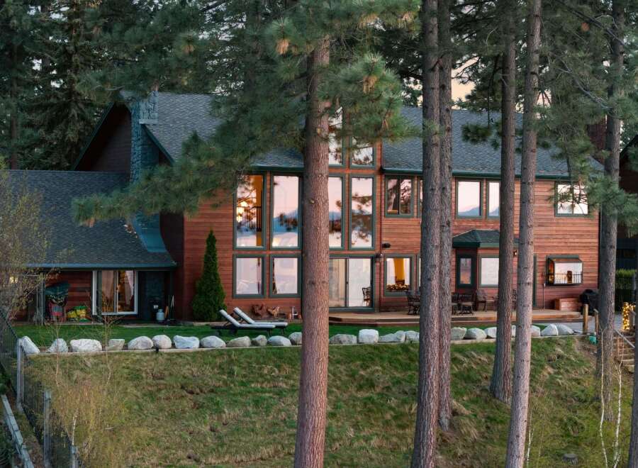 Nestled among towering pine trees, this stunning wooden lodge-style home offers breathtaking views through its expansive windows.